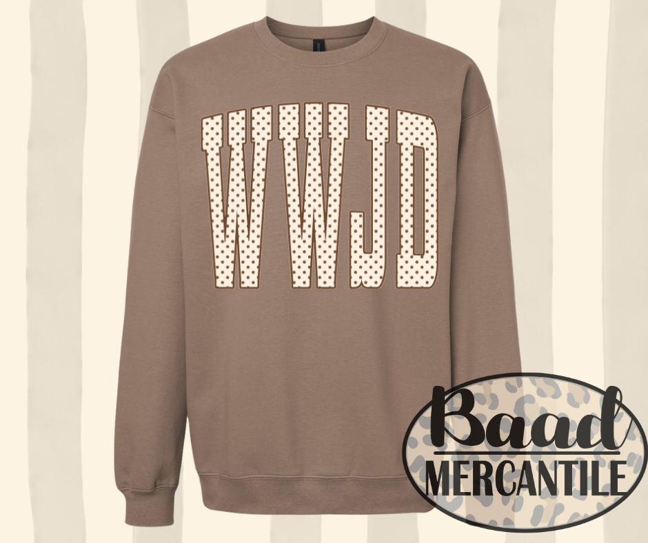 A taupe brown crewneck sweatshirt featuring the letters 'WWJD' in a beige and black polka dot pattern across the chest. The sweatshirt is displayed against a cream and beige vertical striped background, with a 'Baad Mercantile' logo overlay in the bottom right corner.