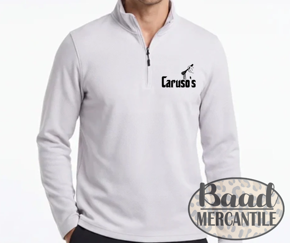 A man wearing a white quarter-zip pullover sweatshirt with a black 'Caruso's' logo printed on the left chest. The image features a 'Baad Mercantile' watermark overlay in the bottom right corner.