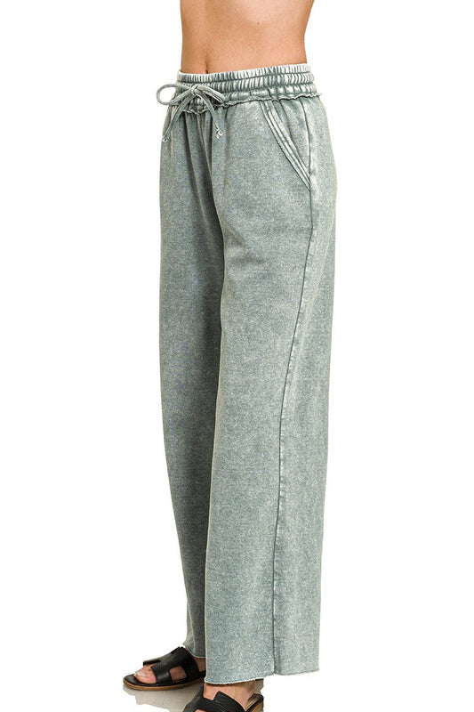 A person wearing wide-leg drawstring pants in a heathered sage green shade, paired with black slide sandals, shown against a plain white background. The text 'ASH JADE' appears in the bottom right corner.